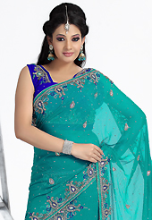 Look stunning rich with dark shades and floral patterns. This turquoise green and royal blue faux chiffon lehenga style saree have beautiful embroidery patch work which is embellished with stone and cutdana work. Fabulous designed embroidery gives you an ethnic look and increasing your beauty. Matching blouse is available. Slight Color variations are possible due to differing screen and photograph resolutions.